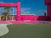 a basketball court on a bright pink building with white windows and a parking lot area