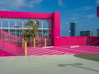 man walking on asphalted court in front of a pink building and stairs with palm trees