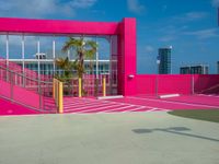 man walking on asphalted court in front of a pink building and stairs with palm trees