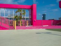 man walking on asphalted court in front of a pink building and stairs with palm trees
