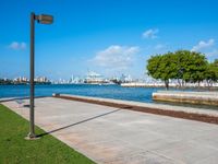 a grassy, cement pathway leading to the water's edge near a park area and beach