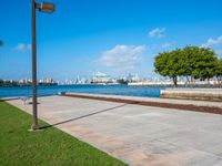 a grassy, cement pathway leading to the water's edge near a park area and beach