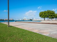 a grassy, cement pathway leading to the water's edge near a park area and beach