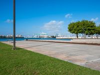 a grassy, cement pathway leading to the water's edge near a park area and beach