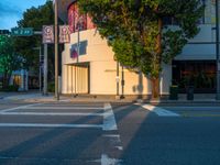 a crosswalk next to a business with buildings in the background at dusk on the city street