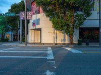 a crosswalk next to a business with buildings in the background at dusk on the city street