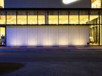 a very large white building lit by some lights from outside the windows as people walk by it