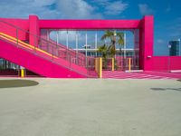 a bright pink building is located by the sea with stairs leading up to it's entrance