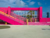 a bright pink building is located by the sea with stairs leading up to it's entrance