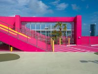 a bright pink building is located by the sea with stairs leading up to it's entrance