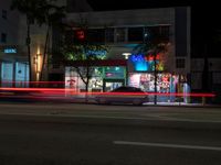 a street with a lit store on the side of it at night next to some tall buildings