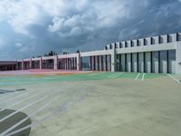 a parking lot that has some big windows and some cars in front of it, on top of a cloudy sky