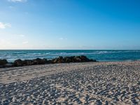 there are many rocks and sand on this beach side lot, with sea waves rolling in and a blue sky above