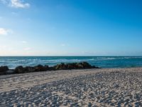 there are many rocks and sand on this beach side lot, with sea waves rolling in and a blue sky above