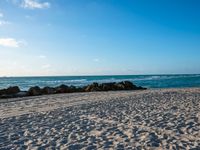 there are many rocks and sand on this beach side lot, with sea waves rolling in and a blue sky above