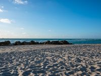 there are many rocks and sand on this beach side lot, with sea waves rolling in and a blue sky above