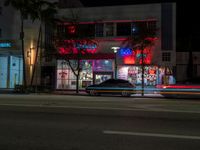 a night view of some shops across from a street car passing by at night time