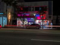 a night view of some shops across from a street car passing by at night time