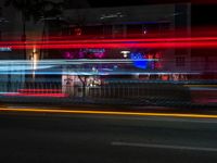 a night view of some shops across from a street car passing by at night time