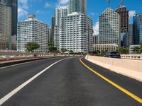 the empty road with lots of skyscrapers in the background with cars driving on the roadway