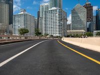 the empty road with lots of skyscrapers in the background with cars driving on the roadway