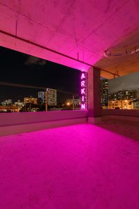 a big window with neon lights above a city skyline at night time, and pink light on the floor