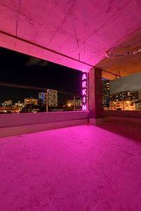 a big window with neon lights above a city skyline at night time, and pink light on the floor