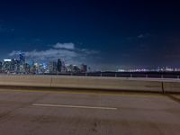 an empty street with a view of the city skyline by night in the background at a bridge