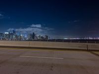 an empty street with a view of the city skyline by night in the background at a bridge