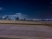 an empty street with a view of the city skyline by night in the background at a bridge