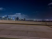 an empty street with a view of the city skyline by night in the background at a bridge