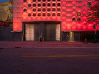 a large building that is red lit up at night with a red light shining on the side