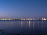 the skyline lights up in the blue night sky in this wide view of a harbor