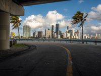 view of buildings, skyscrapers and palm trees near the water from under a street bridge