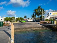 a boat going across water with palm trees and other buildings in the background and one green car on a long drive