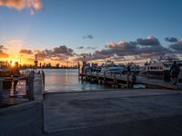 a sunrise over the ocean with many boats parked near by a dock and a city skyline in the distance