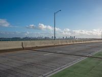 a green area next to a highway next to the ocean with an overpass and street lights on a sunny day