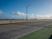 a green area next to a highway next to the ocean with an overpass and street lights on a sunny day