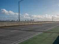 a green area next to a highway next to the ocean with an overpass and street lights on a sunny day