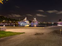 two boats docked next to each other in a marina at night time, with some lights on