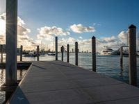 boats are moored at the harbor near a pier with posts sticking out into the water