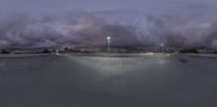 a cloudy sky hangs over the parking lot of the commercial center at night with a skateboard ramp at the front