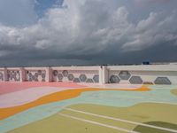 the sky is dark and cloudy over the large building and wall paint that was painted by children