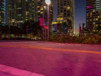 a purple glow from a street light over a street with tall buildings in the background