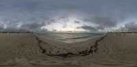 a fisheye lens picture of a beach and sky with clouds overhead at sunset near a body of water