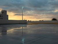 a parking lot in front of an industrial building at sunset with the sky reflecting off of it