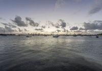 boats in the water as the sun rises on a cloudy day, with small clouds above them