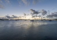 boats in the water as the sun rises on a cloudy day, with small clouds above them