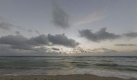 the view of a beach from an ocean side cliff at sunset in india, with clouds and sun shining on the horizon