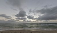 the view of a beach from an ocean side cliff at sunset in india, with clouds and sun shining on the horizon